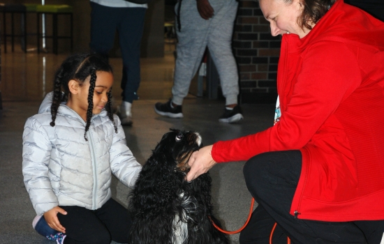 A young girl pets a therapy dog while the handler watches