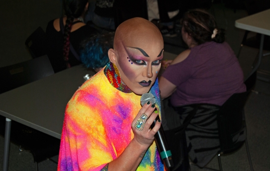 Drag queen Sabin speaks to the crowd through a microphone while looking into the camera