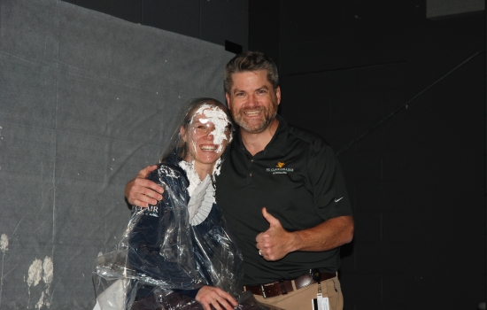 A man and whipped cream-covered faculty member smile together for a photo