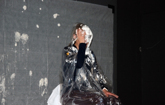 A faculty member covered in whipped cream sits on a chair 
