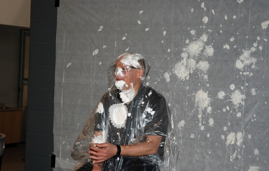 A whipped-cream covered faculty member sits in a chair 