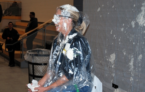 A whipped-cream covered faculty member sits in a chair 