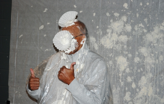 A faculty member with pies all over his face gives two thumbs up