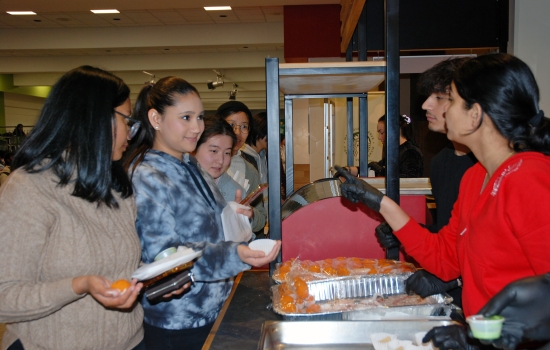 Harnoor and student staff hand out treats at the Grab N' Go Kiosk to a line of hungry students