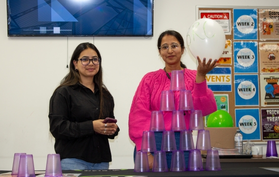 Volunteer lead and a student holding a balloon stand behind a table with a full tower of stacked plastic cups