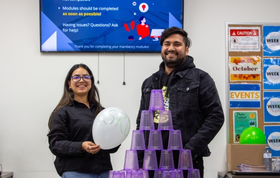Volunteer lead holding a balloon and a student stand behind a table with a full pyramid of stacked cups