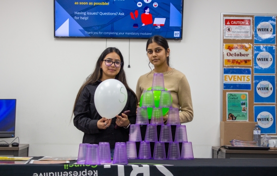 Volunteer lead and a student both hold balloons standing behind a table with a full tower of stacked cups