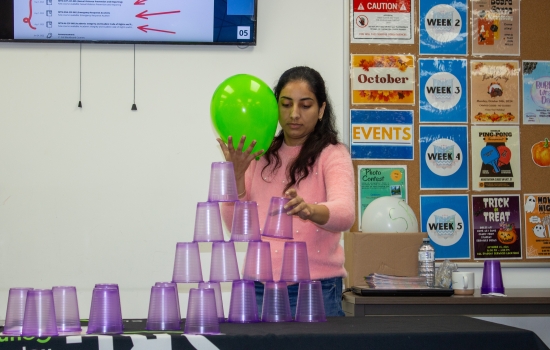 A student attempts to stack cups while keeping a balloon up in the air