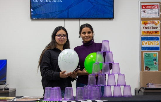 Volunteer lead and a student both hold balloons standing behind a table with a full tower of stacked plastic cups