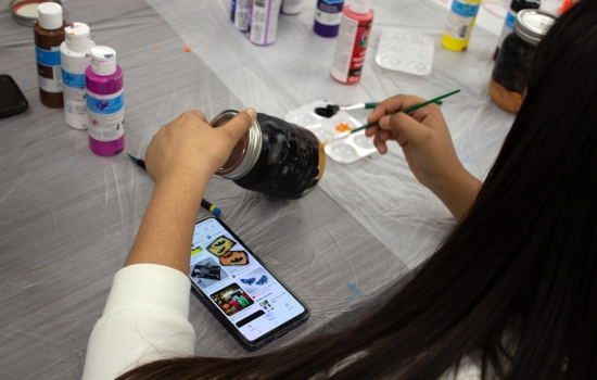 A POV of a student painting a jar with a reference image on her phone