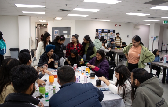 A group shot of students sitting at tables painting jars