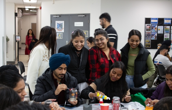 A group shot of students sitting at tables painting jars