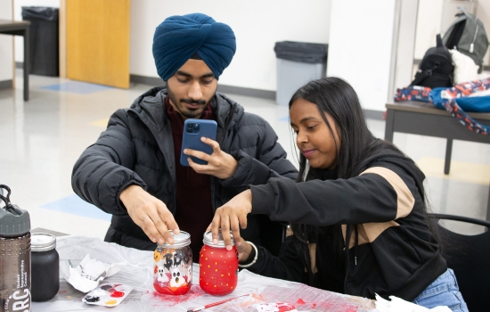 Two students take photos of their painted jars with their phones
