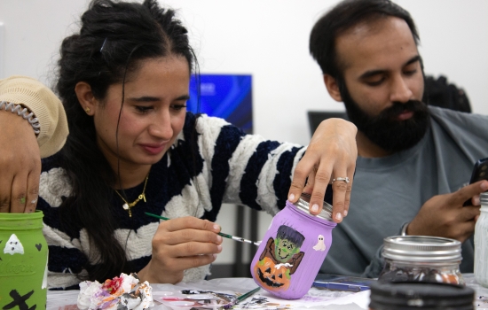 A student in a striped shirt sits at a table painting a jar 
