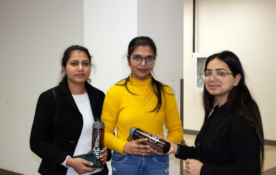 Two students pose for a photo with Sakshi as she hands one of them an SRC water bottle