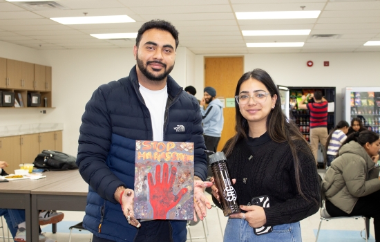 A students shows off his art piece for the camera while Sakshi holds an SRC water bottle to give him