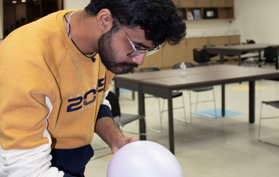 A student uses a balloon to attempt to blow the cards off the water bottle