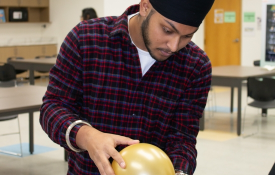 A student uses a balloon to attempt to blow the cards off the water bottle