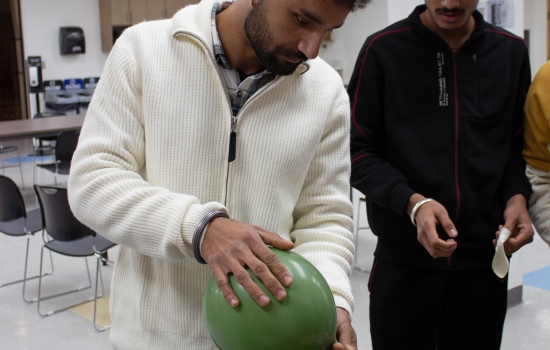 A student uses a balloon to attempt to blow the cards off the water bottle
