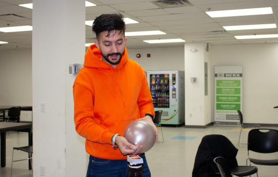 A student uses a balloon to attempt to blow the cards off the water bottle