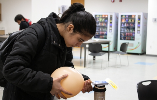 A student uses a balloon to attempt to blow the cards off the water bottle