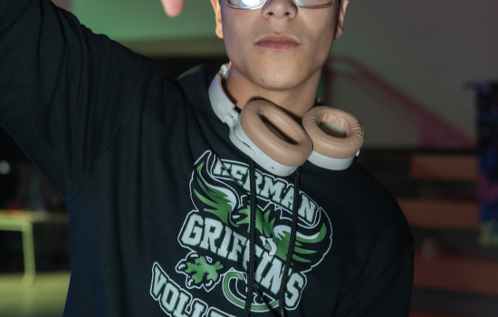 A student wearing headphones and glasses poses for the camera