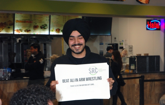 Pratham holds up a sign that says "Beat Ali in arm wrestling"