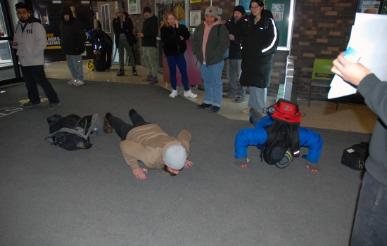 Two students do pushups near the front doors of the college
