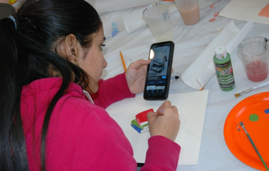 A student looks at a reference on their phone as they paint