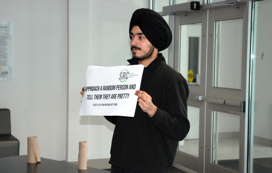 Pratham holds up a sign that says "approach a random person and tell them they are pretty"