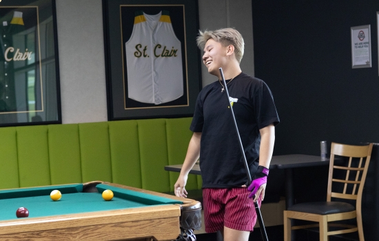 A participant holding a pool cue and leaning on the table smiling