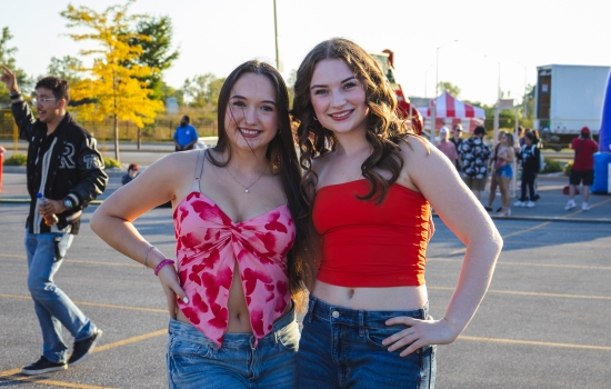 two college students smile and pose for the camera with a carnival in the background