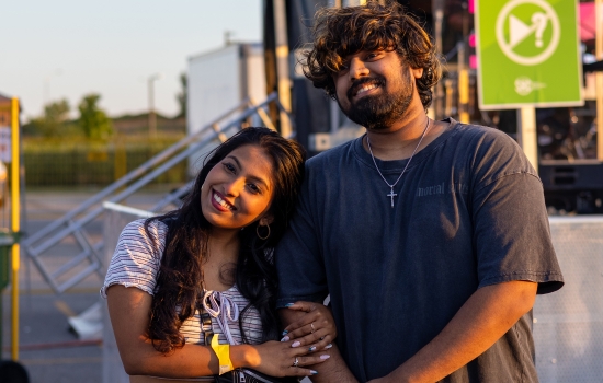 Two college students smile and pose for the camera with a carnival in the background