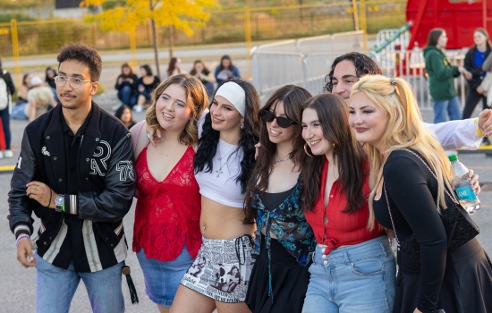 A group of college students smile and pose for the camera with a carnival in the background