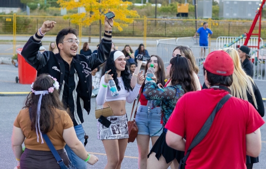 college students dance in a parking lot with a carnival in the background