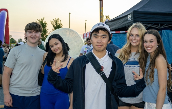 a group of college students smile and pose for the camera with a carnival in the background