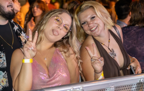 Two students smile and pose in front of a stage barrier
