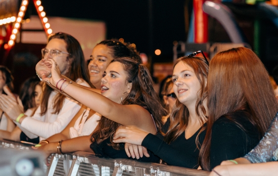 A concert crowd dances in front of a stage barrier 