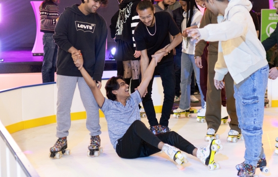 A student falls on the rink as his friends try to help him up
