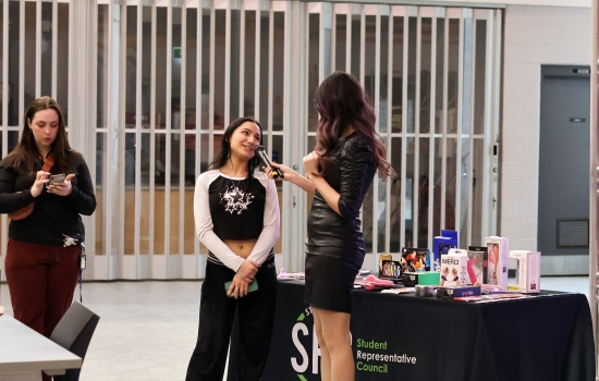 A student speaks into a microphone held by Alisha