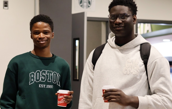 Two students pose for a photo holding their coffees