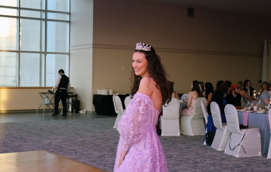 A guest wearing a purple dress and tiara smiles