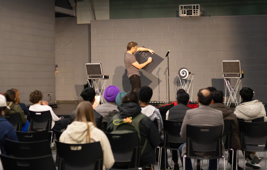 Eric Leclerc writes on a board on the stage in front of an audience