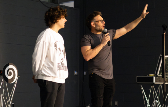 Eric Leclerc speaks into the mic on stage with a student with him