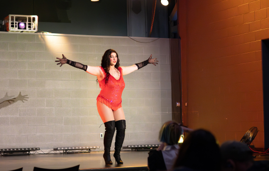 Drag queen remedy performs in tall black boots and a red bodysuit