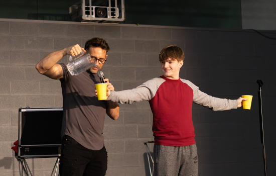 Eric Leclerc and a student volunteer on stage. The student is holding two yellow cups while Eric pours water into one