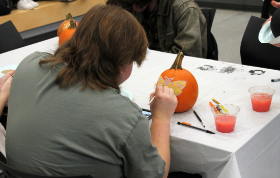 A student painting a moth on a pumpkin