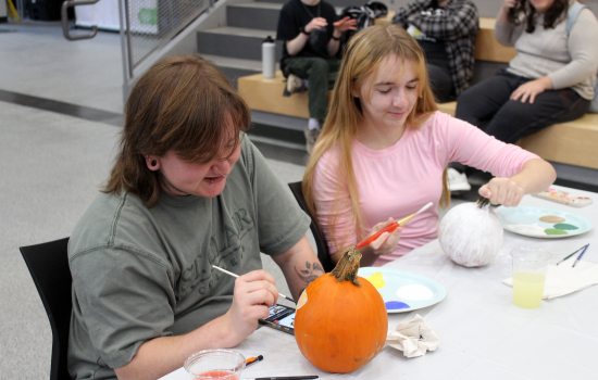 Two students smile while painting their pumpkins