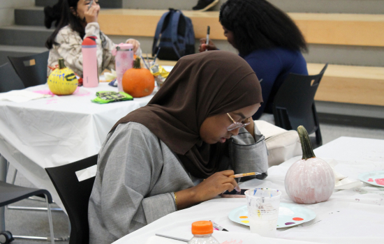 A student sitting at a table looks at a reference for pumpkin painting