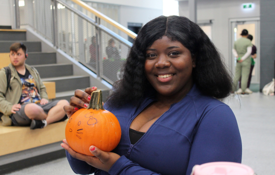 A smiling student shows off her painted pumpkin in the SLC
